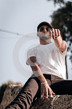 Vertical shot of a stylish caucasian boy sitting on a rock and posing with his hand put forward