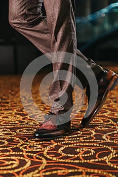 Vertical shot of a stylish man in textured brown suit pants and brown and black brogue shoes