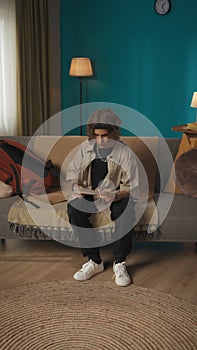 Vertical shot of a teenager, young man sitting on a sofa, couch, reading a document, paper, admission, waiting to see