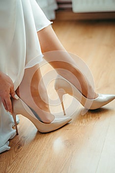 Vertical shot of the tender hands of the bride are putting on the white wedding high heels.