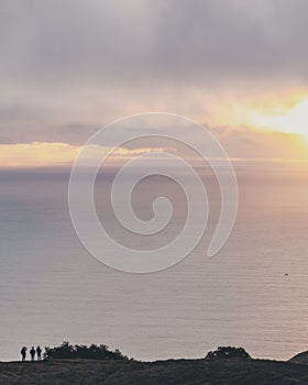 Vertical shot of three people standing in the distance looking at the beautiful sea