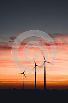 Vertical shot of three wind turbines isolated on the background of the pink sky