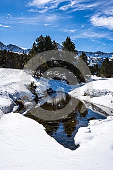 Vertical shot of tiny lake in the middle of snowy fields and green trees in Andor