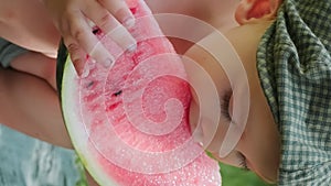 Vertical shot. Toddler boy eating watermelon outdoors. Summer food.