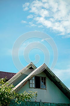 Vertical shot of the top of an old house with broken glass window against blue sky