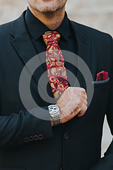 Vertical shot of the torso of a man in a black suit and shirt with red paisley tie