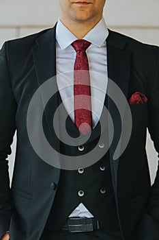 Vertical shot of the torso of a man in a black suit and white shirt with a maroon tie