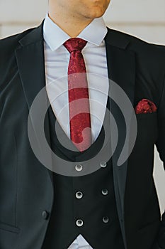 Vertical shot of the torso of a man in a black suit and white shirt with a maroon tie