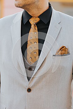 Vertical shot of the torso of a man in a light gray suit and black shirt with brown tie