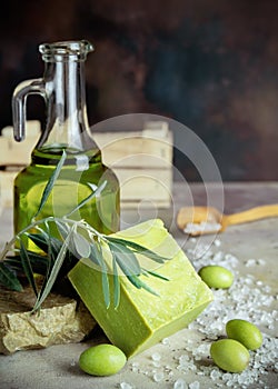 Vertical shot of traditional natural organic olive soap. Handmade soap bar, green olives, leaves, glass jar of olive oil and a