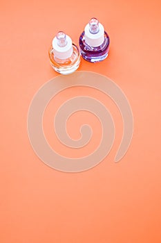 Vertical shot of two bottles of essential oil on a peach-colored surface