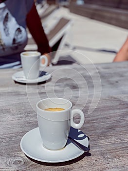 Vertical shot of two espressos in white cups on a wooden table in sunlight