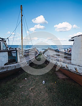 Vertical shot of two fishing boats out of the water and on a beach under the blue sky