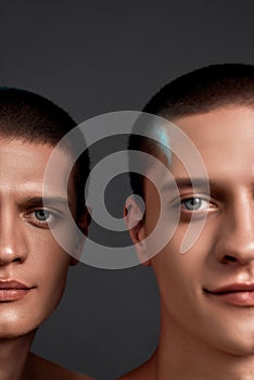 Vertical shot of two young caucasian twin brothers looking at camera and smiling, posing together isolated over grey