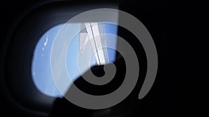 Vertical shot of unrecognizable male hand closing curtain of window in airplane overlooking airplane wing and blue sky