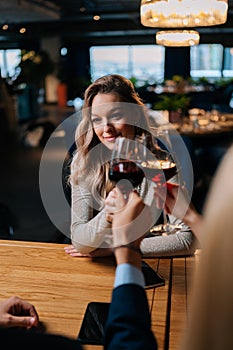 Vertical shot of unrecognizable man and woman clinking glass of red wine with pretty blonde female sitting at table in
