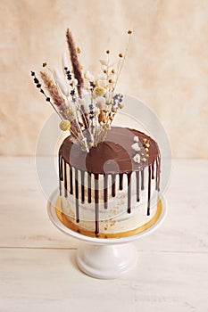 Vertical shot of a vanilla cake with chocolate drip and flowers on top