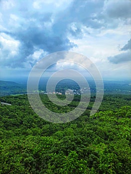 Vertical shot of vast forests with a rural settlement seen from afar and the cloudy sky above