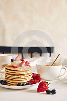 Vertical shot of vegan pancakes with colorful fruits ner a coffee and syrup