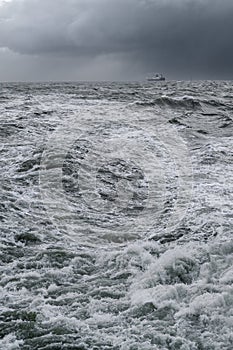 Vertical shot of very rough sea with black dramatic clouds in the sky and small ship on the horizon. Storm at the sea