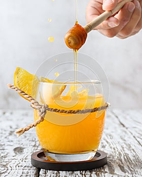 Vertical shot of a vibrant orange drink with a man's hand as he drizzles honey on it