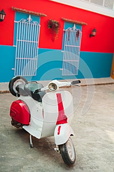 Vertical shot of a vintage Vespa scooter parked in front of a red and blue wall