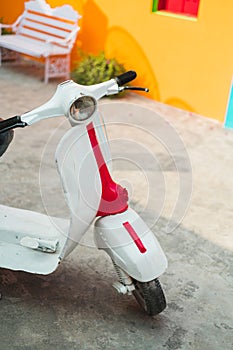 Vertical shot of a vintage Vespa scooter parked in front of a yellow wall