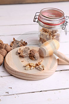 Vertical shot of walnuts in a jar and on a wooden cutting board on the table with a small hammer