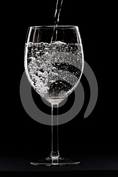 Vertical shot of  water being poured in a transparent glass isolated on a black background