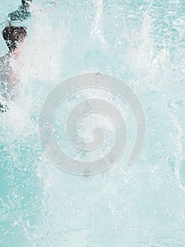 Vertical shot of water slashing from a boy jumping in a pool on a summer day.