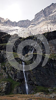 Vertical shot of a waterwall falling from the mountains with high cliffs in the background