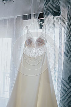 Vertical shot of a wedding dress hanging from the blinds.