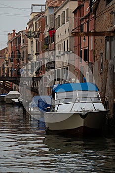 Vertical shot of a white boat in a canal surrounded by low-rise old buildings of Venice, Italy