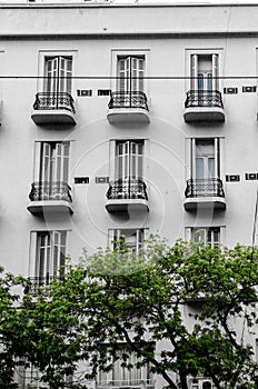 Vertical shot of a white building with balconies in rows with green trees below