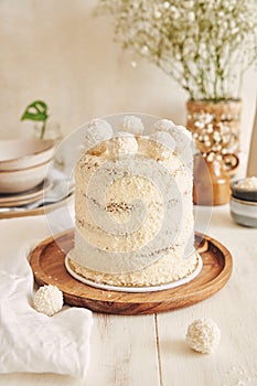 Vertical shot of a white creamy cake with coconut flakes on a round wooden tray on a table