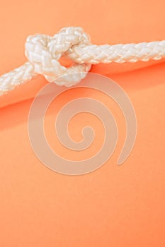 Vertical shot of a white rope with a knot isolated on the pastel orange background