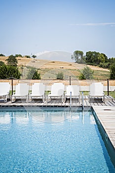 Vertical shot of white summer loungers by a swimming pool surrounded by trees under a blue sky