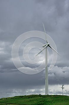 Vertical shot of wind power turbines in a field under the cloudy dark sky
