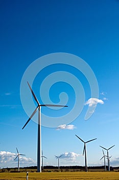 Vertical shot of wind turbines in a field in the countryside under a bright blue sky