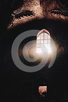 Vertical shot of a window with light shining into dark basilica building with cherub mosaic details