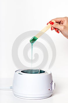 Vertical shot of woman hand holding wooden depilatory spatula, dripping green hot wax into thermostat heater photo