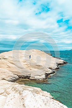 Vertical shot of a woman standing on the white cliff. Sarakiniko. Milos Island, Greece.