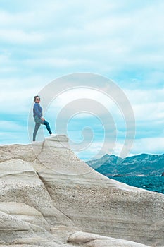 Vertical shot of a woman standing on the white cliff. Sarakiniko. Milos Island, Greece.