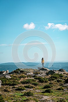 Vertical shot of a woman wearing a yellow jacket on top of a mountain under a blue sky