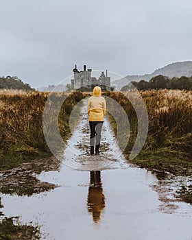 Vertical shot of the woman in a yellow jacket looking at Kilchurn Castle. Dalmally, UK.
