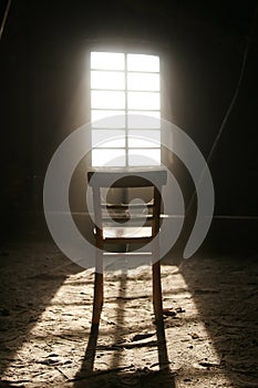 Vertical shot of a wooden chair in an abandoned building at the sunlight of window