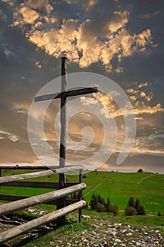 Vertical shot of a wooden cross against the background of the cloudy sky at sunset.