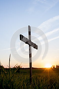 Vertical shot of a wooden cross in a grassy field with the sun shining in a blue sky