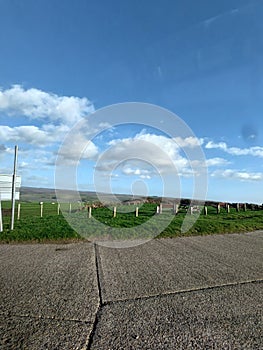 Vertical shot of wooden pilings and bench in lush green field under blue cloudy sky