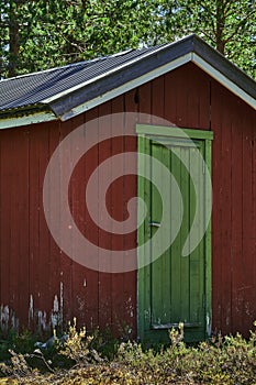 Vertical shot of a wooden red wharehouse with a green door and trees in the background.